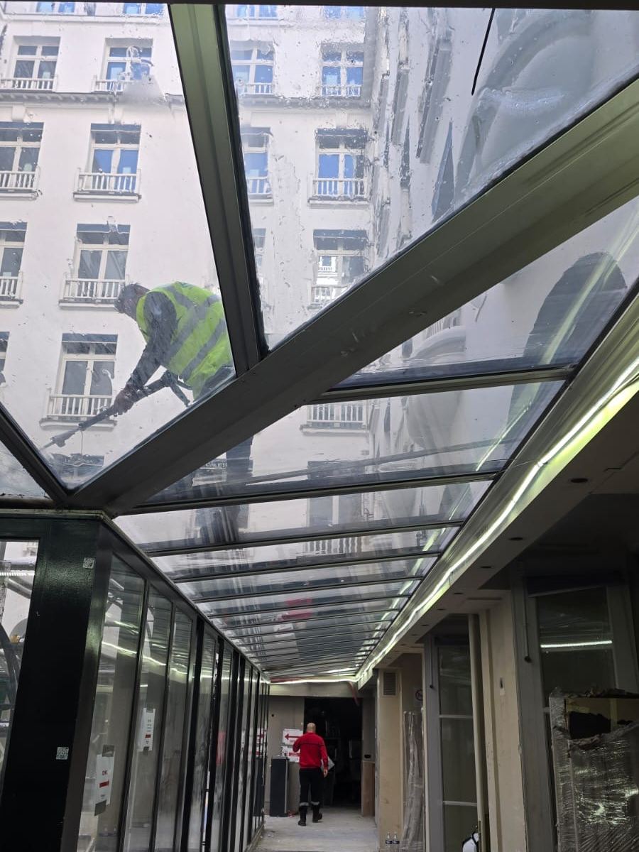 Agent nettoyant la verrière d’un hôtel, vu à travers le vitrage